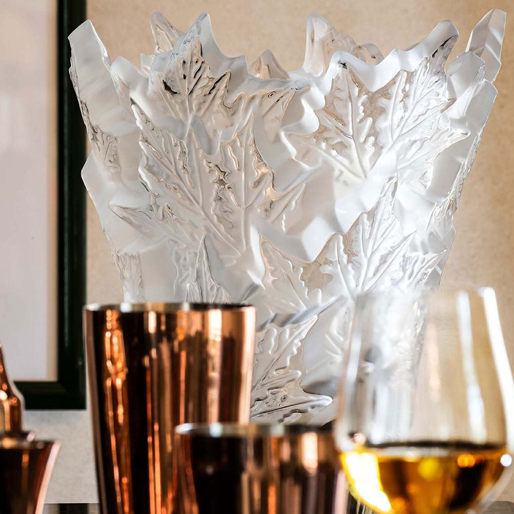 Decorative glass vase with leaf patterns on a table with wine glasses.