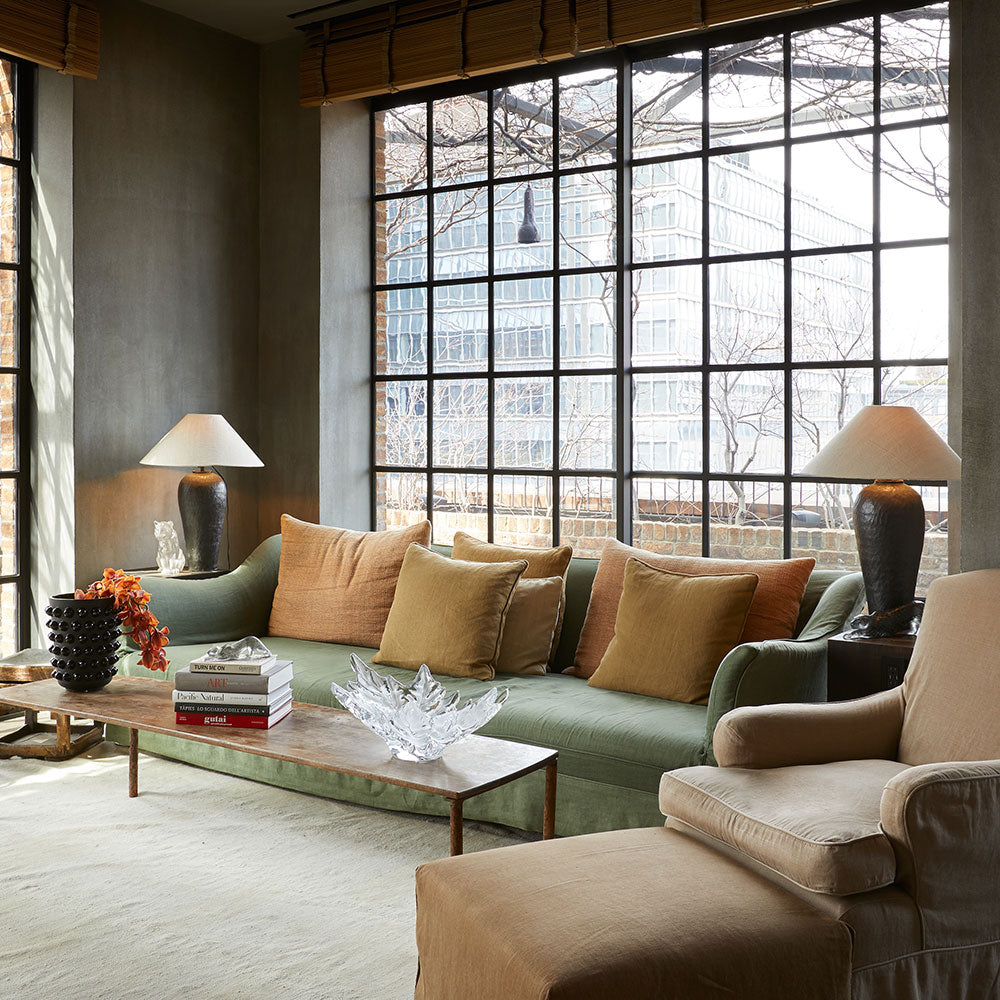 Modern living room with large windows, green sofa, and beige armchair.