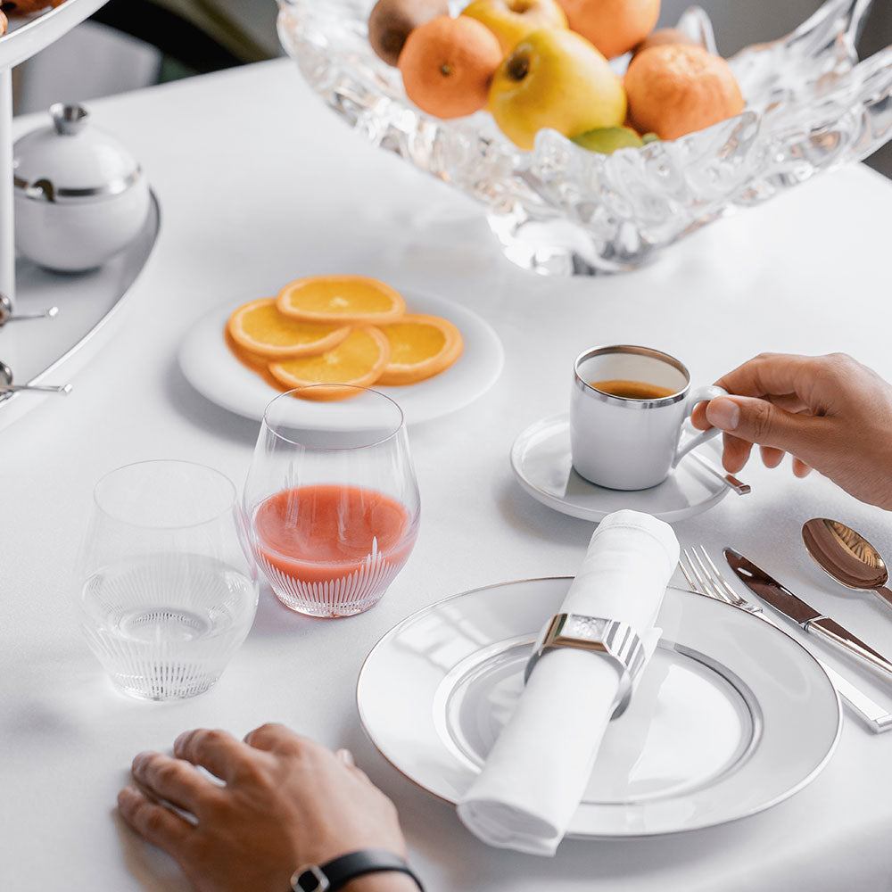 Dining table setting with a cup of coffee, fruit, and cutlery.