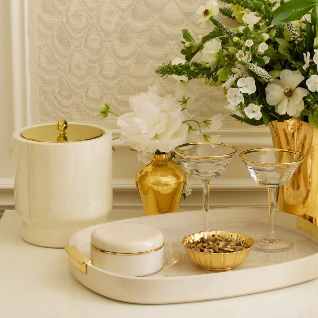 Decorative setting with gold and white items including a vase, bowl, and glasses on a tray.