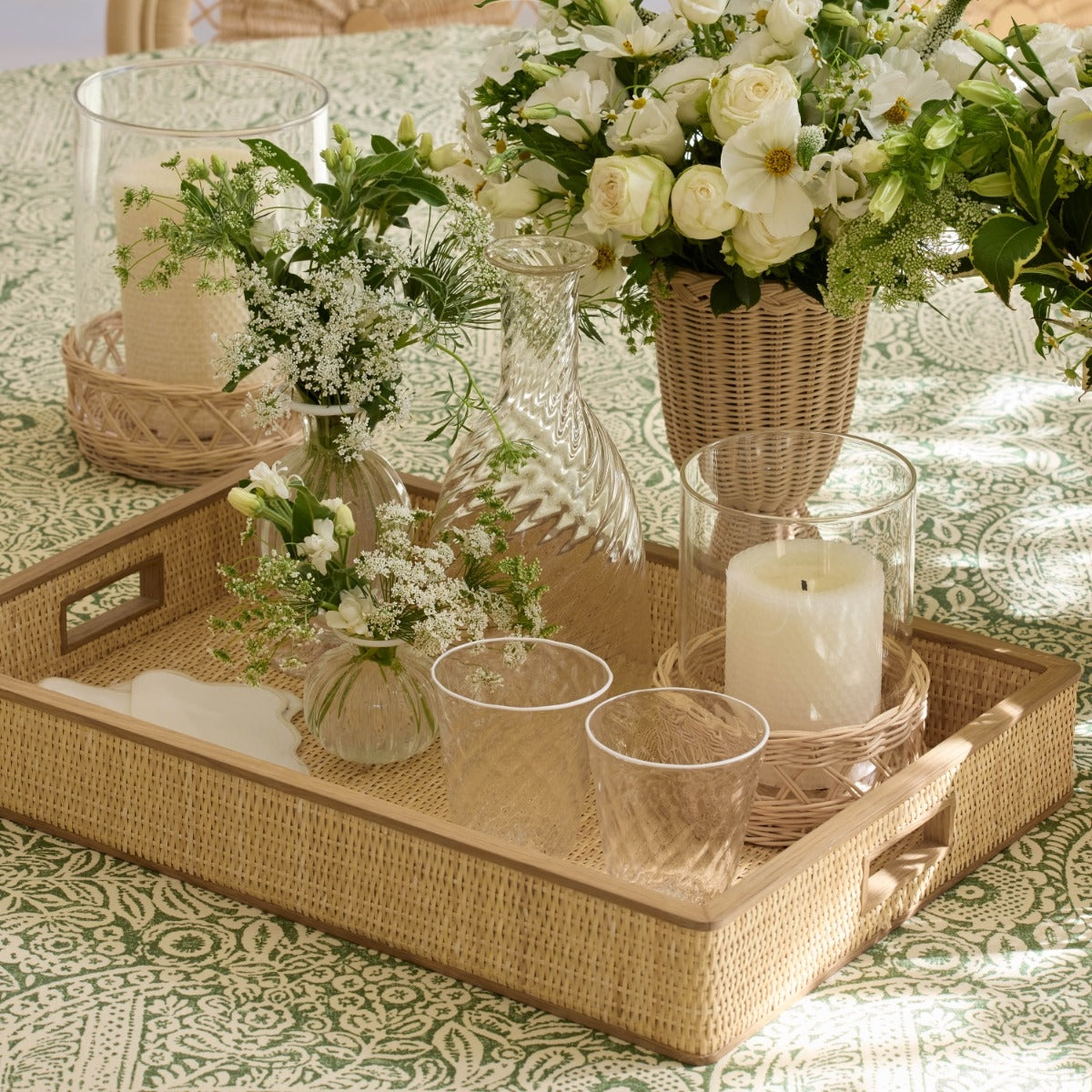 Decorative table setting with candles, glasses, and flowers on a patterned tablecloth.
