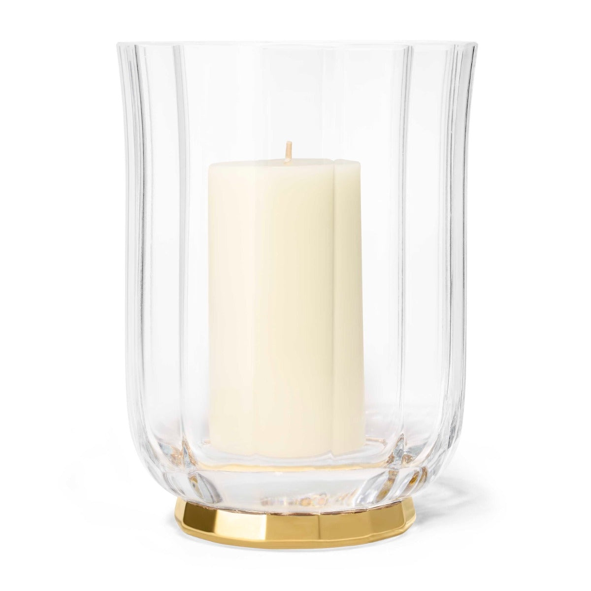 Clear glass hurricane lamp with a gold base and a white candle inside on a white background
