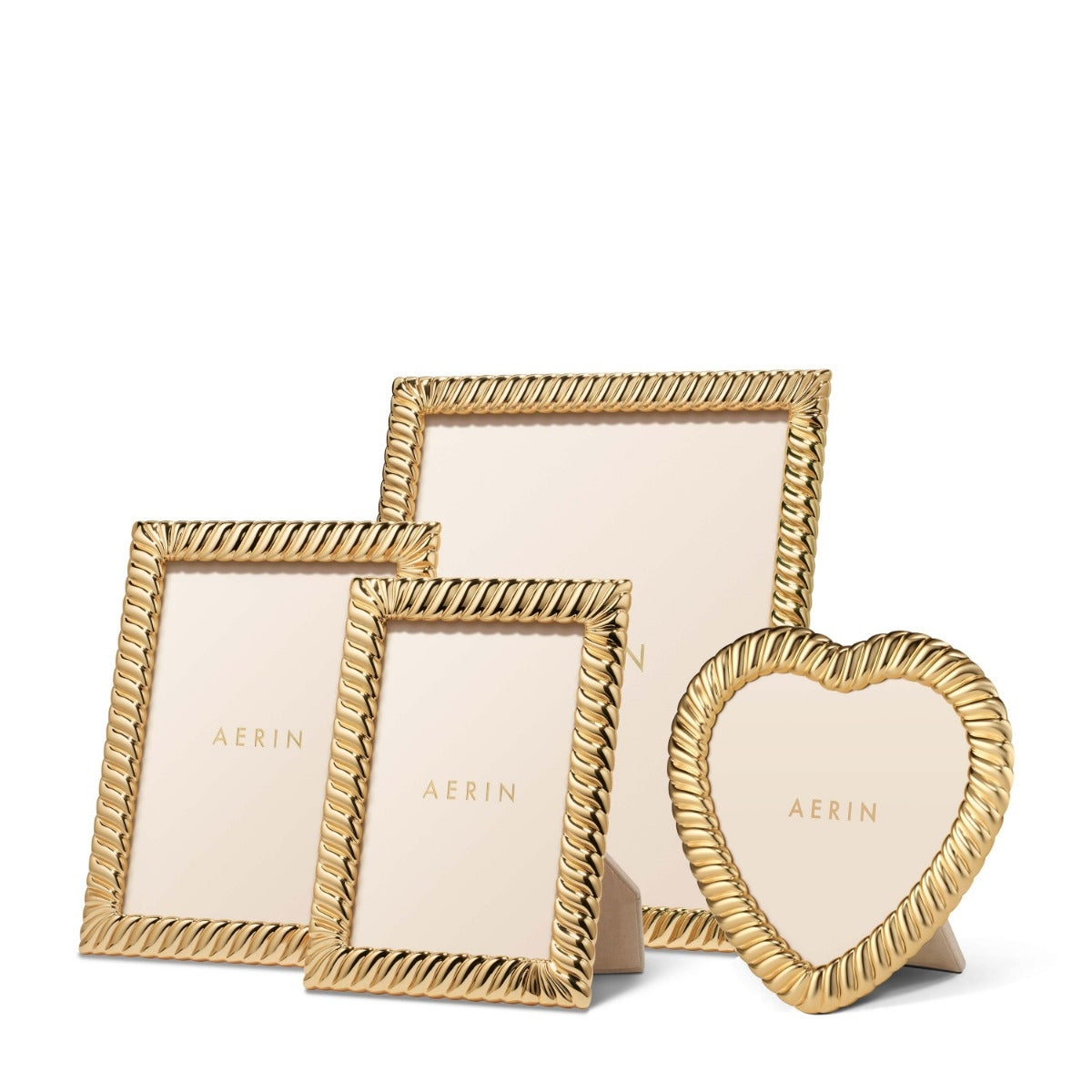 Three gold picture frames by AERIN on a white background: two square frames with twisted rope-style borders and one heart-shaped frame, all shown with pale blush photo inserts.