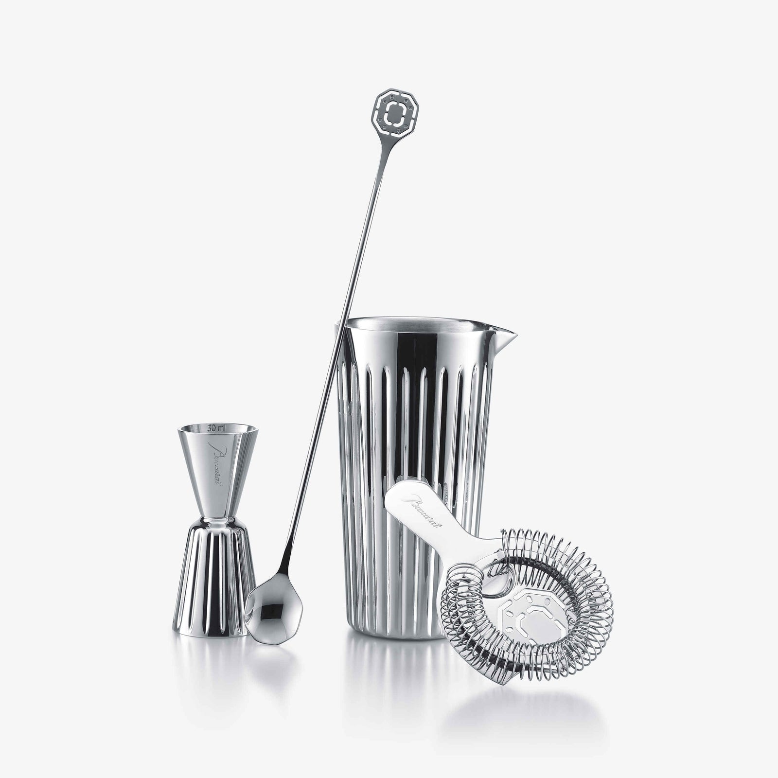 Set of silver cocktail-making tools including a pitcher, jigger, spoon, and strainer on a white background.