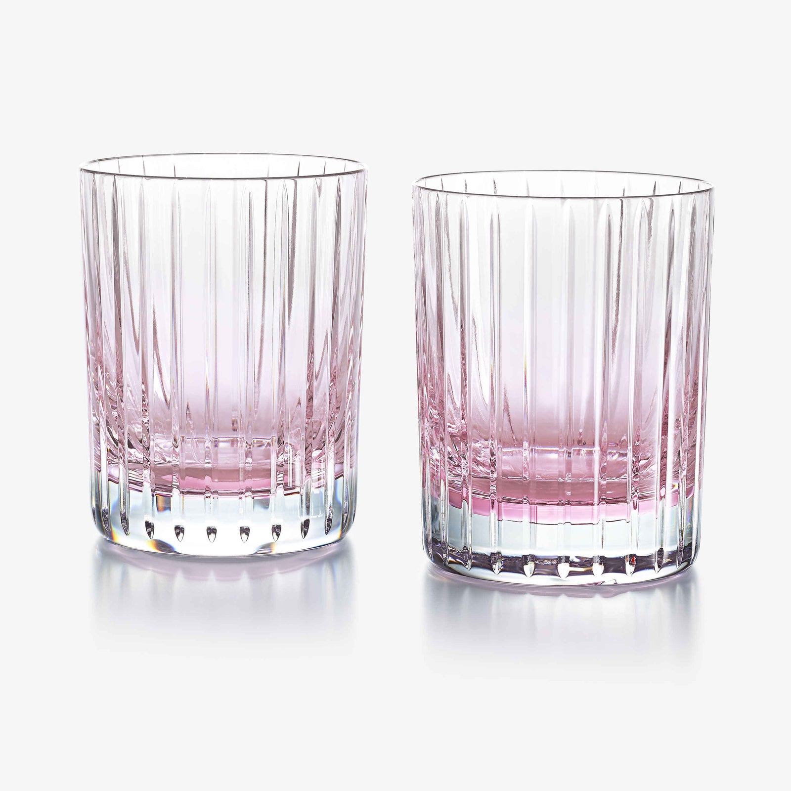Two clear glasses with pink tinted bottoms on a white background