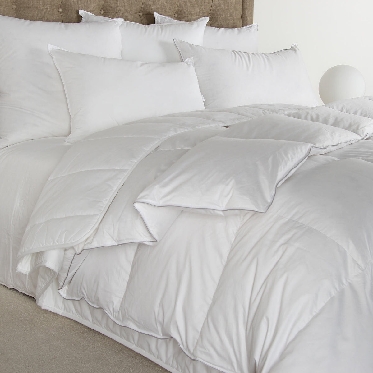 White comforter and pillows on a bed with a neutral headboard.