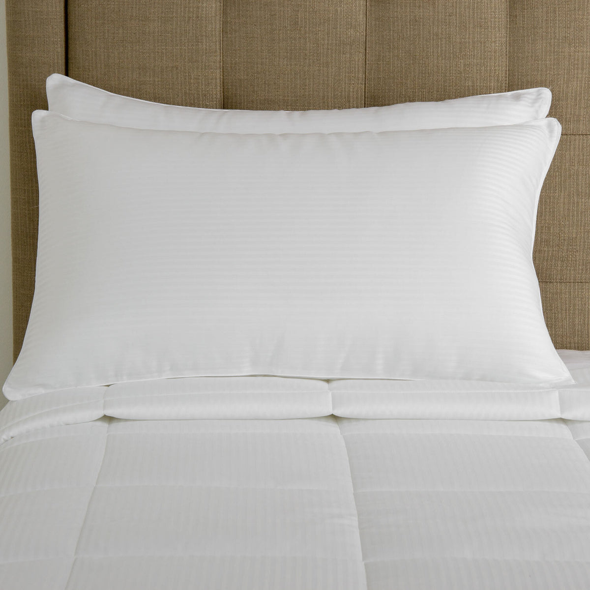Two white pillows on a bed with a beige headboard