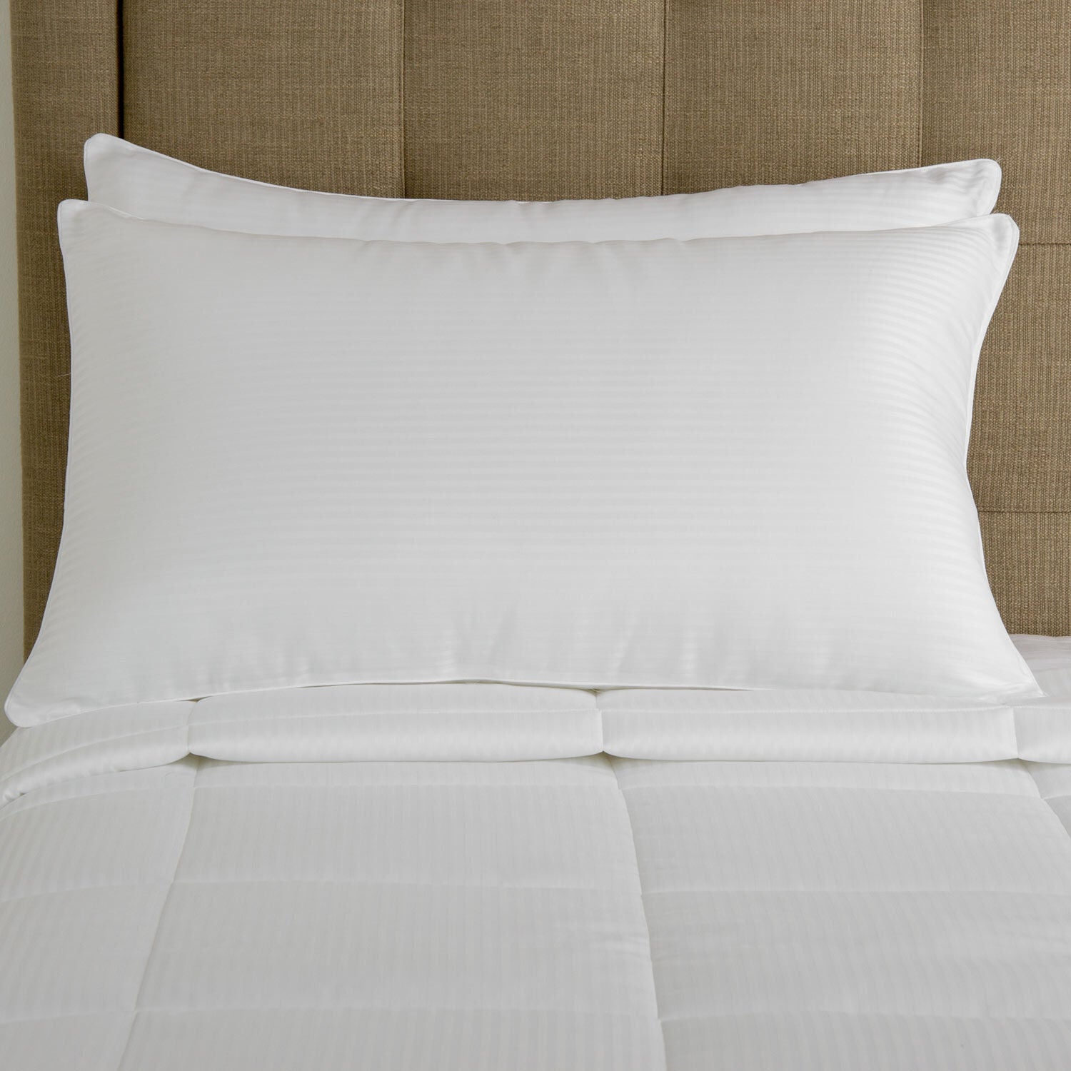 Two white pillows on a bed with a beige headboard