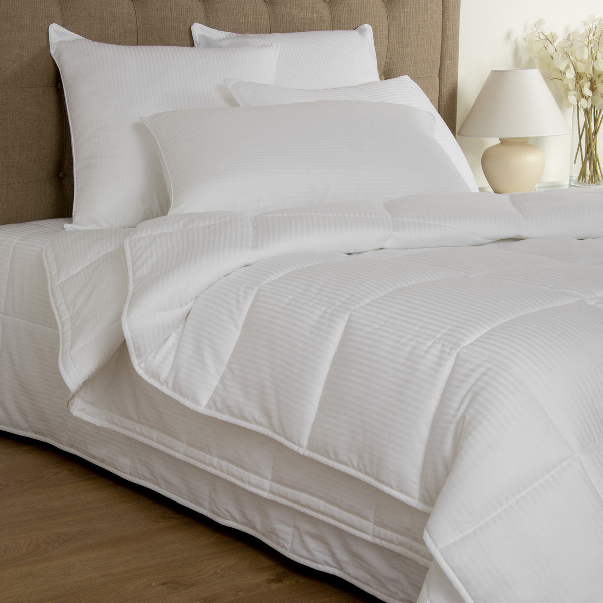 White bedding set on a bed with pillows and a lamp in the background.
