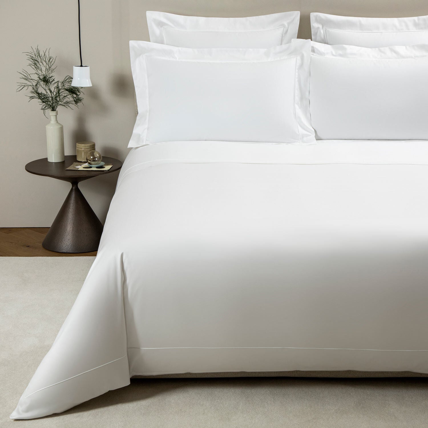 Neatly made bed with white bedding and pillows in a minimalistic room.