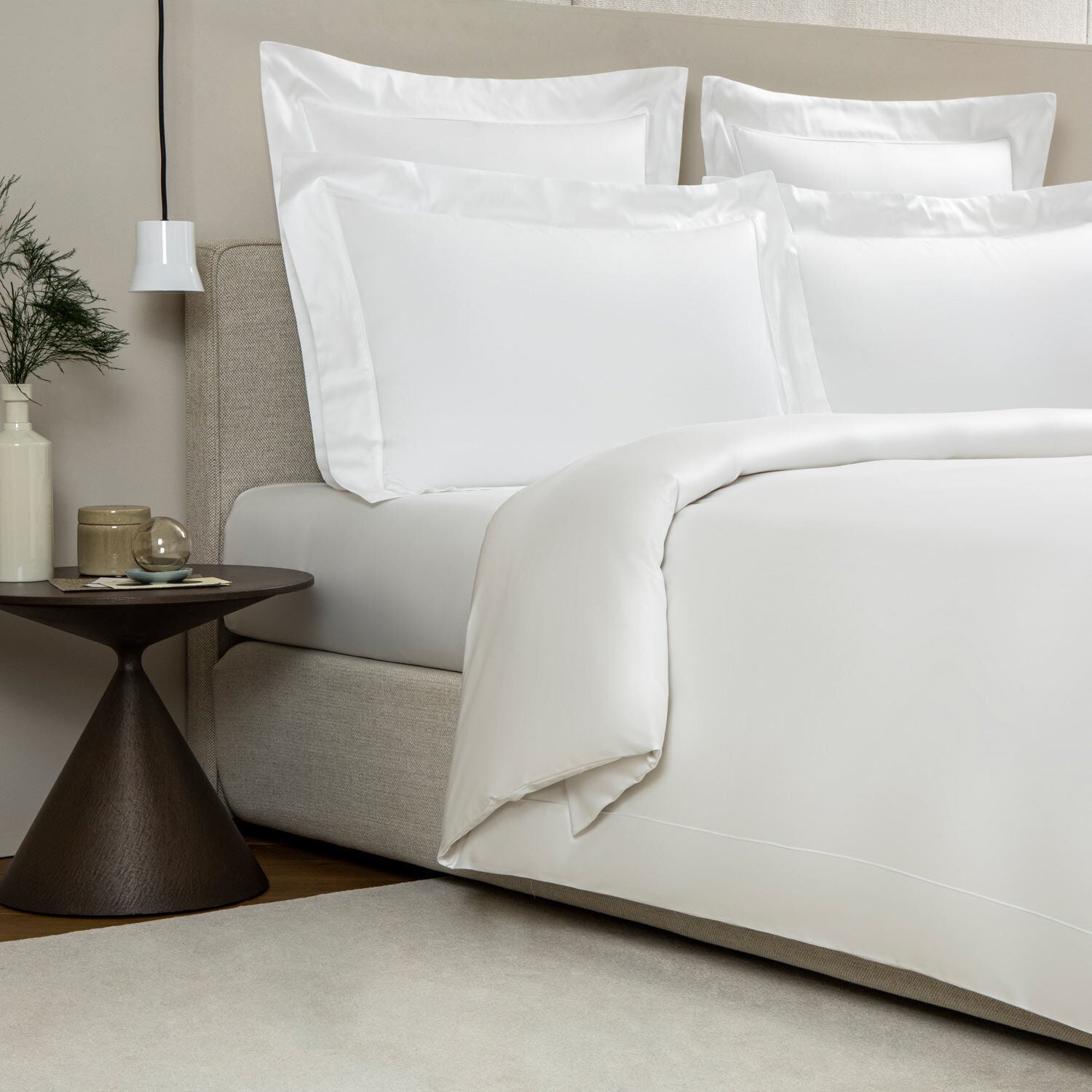 Neatly made bed with white bedding and pillows in a minimalistic room.