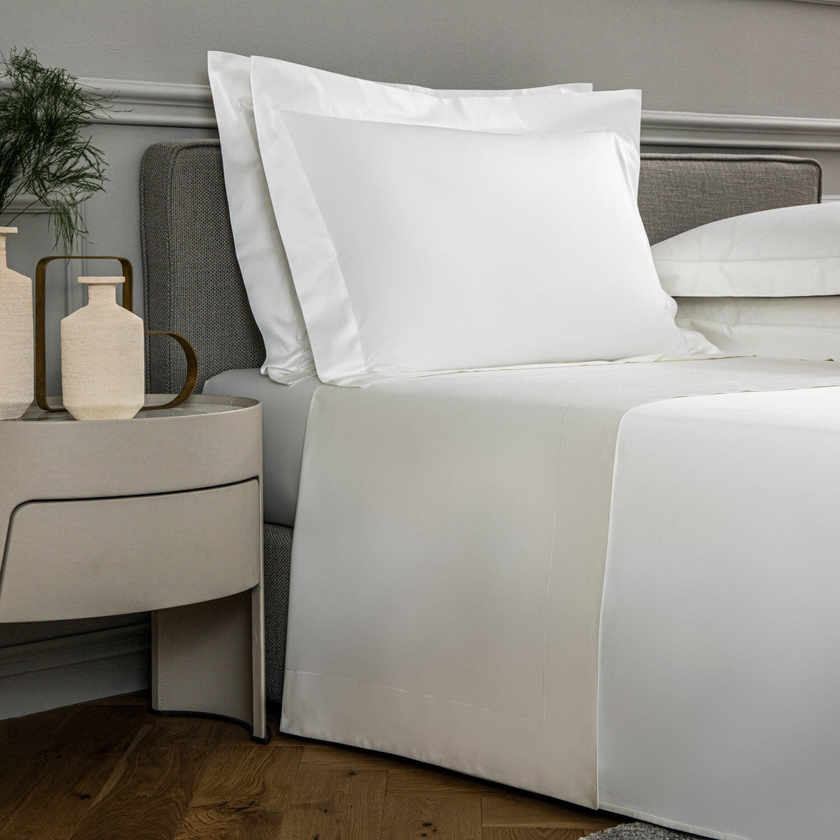 Bedroom with a neatly made bed featuring white bedding and pillows, next to a nightstand with decorative items.