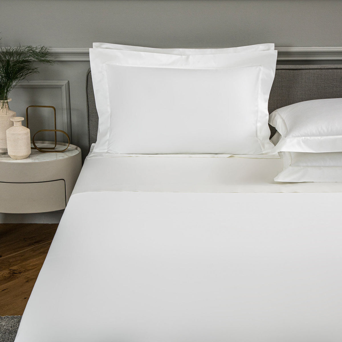 White bed linens, including a flat sheet and two pillowcases, neatly arranged on a bed in a modern bedroom setting.