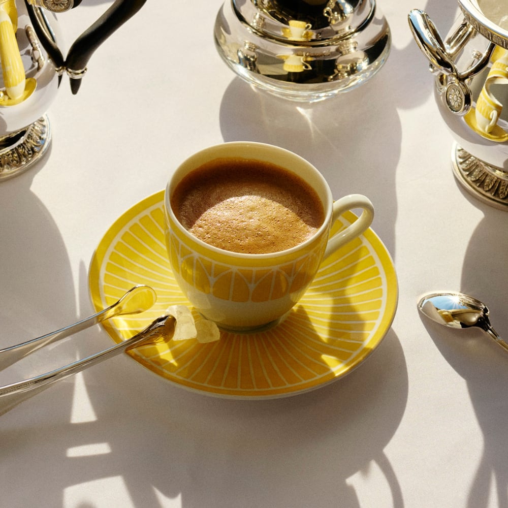 White teacup with yellow interior on a matching saucer against a green background