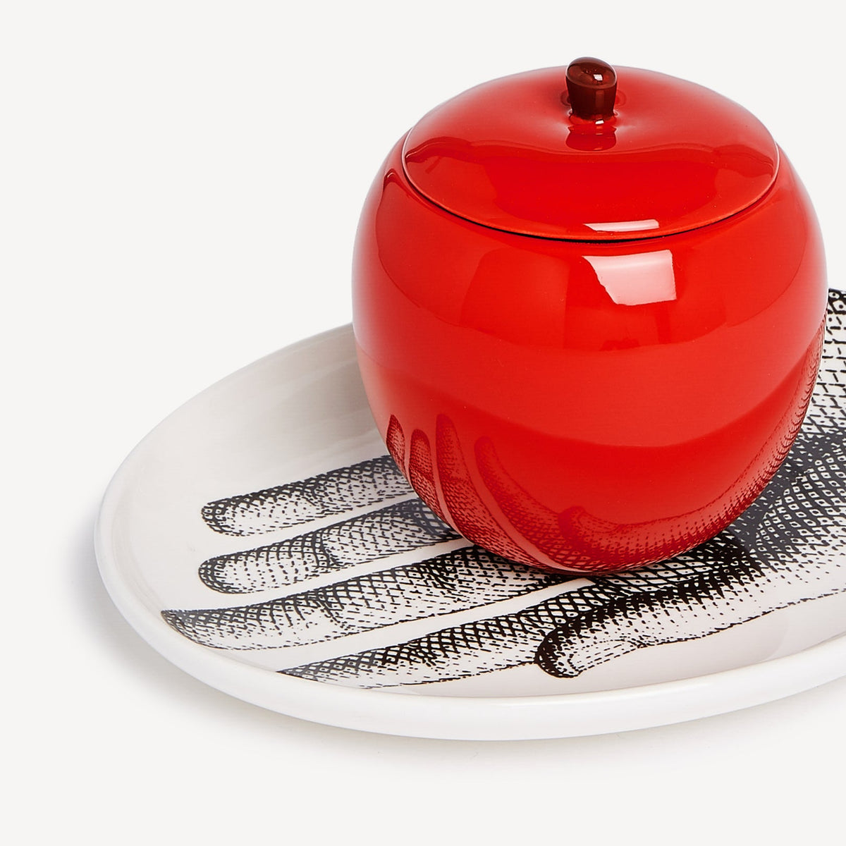 Red ceramic jar with a lid on a decorative plate with feather pattern