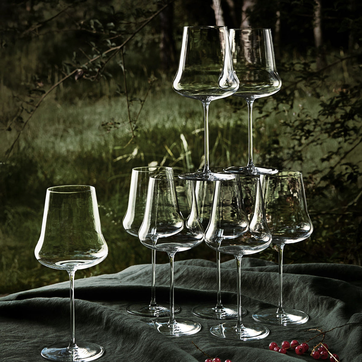 Set of clear wine glasses arranged in a pyramid formation on a dark surface with a natural background.