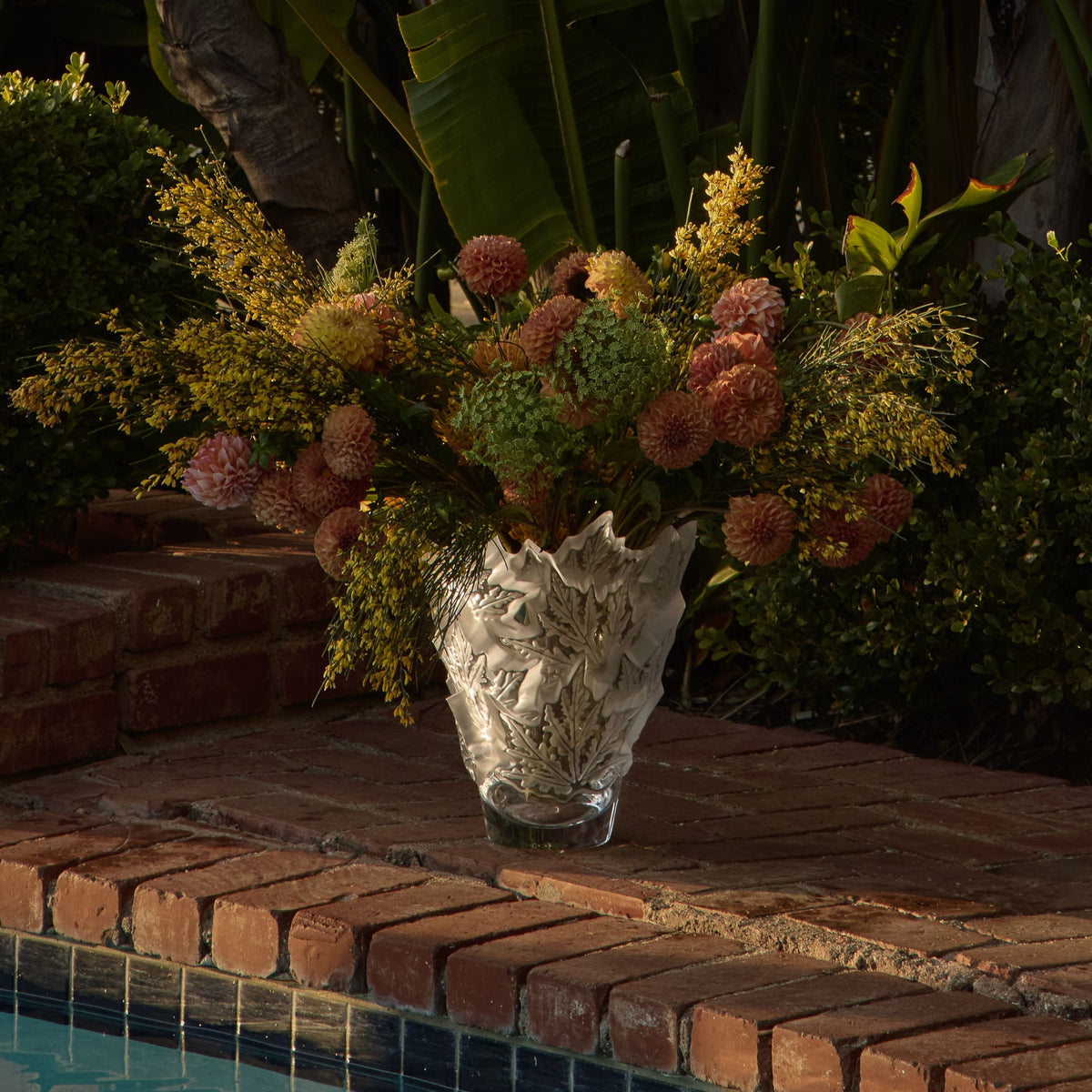 Decorative vase with flowers on a brick ledge by a pool