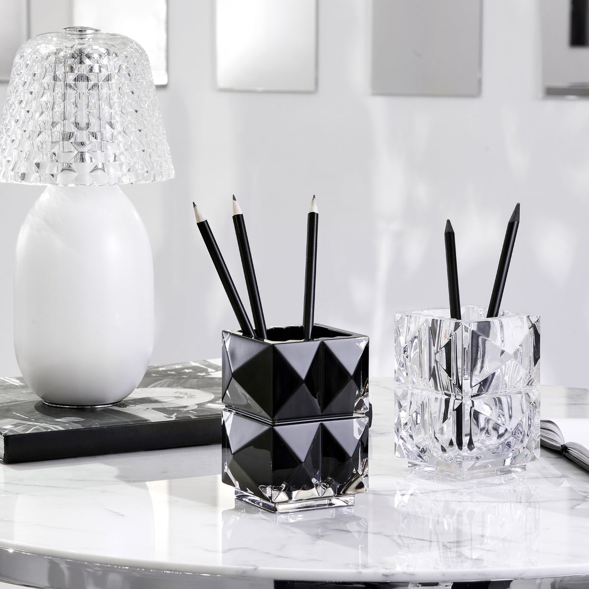 Two geometrically designed pencil holders with black pencils on a marble surface.