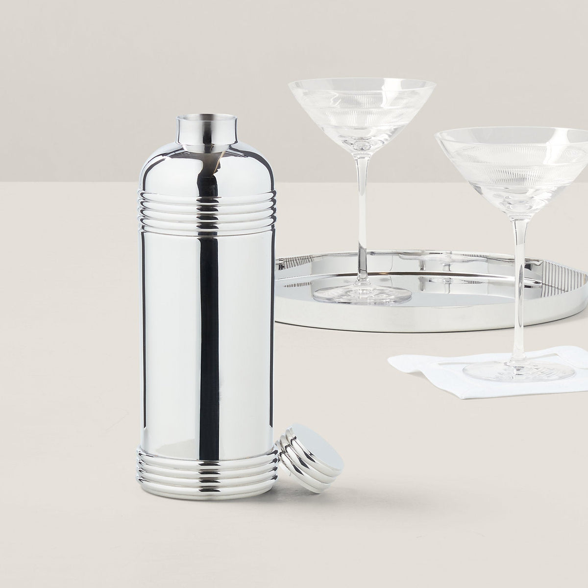 Silver cocktail shaker with two martini glasses on a light background