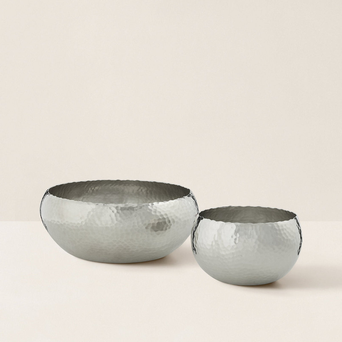 Two silver hammered metal bowls on a beige background