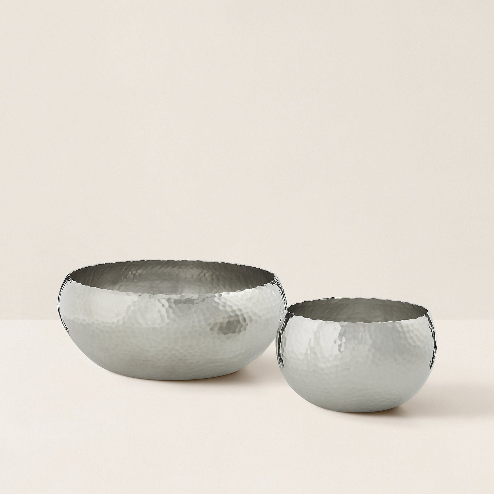 Two silver hammered metal bowls on a beige background