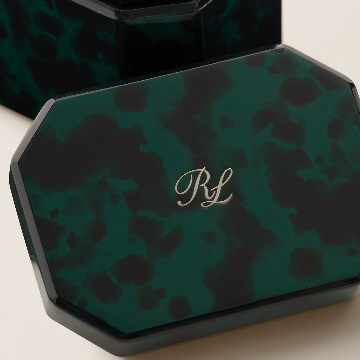 A close-up of a dark green and black marbled or tortoiseshell-patterned octagonal jewelry box, with the lid partially open. The lid features a gold monogram 'RL' in the center.