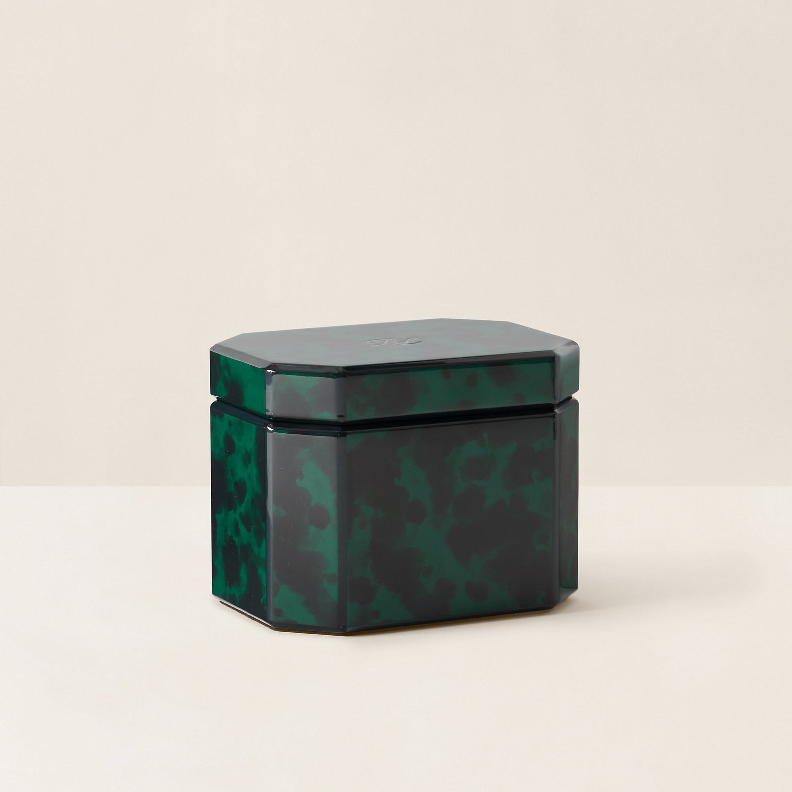 A dark green faceted glass storage jar with a matching lid, featuring a glossy tortoiseshell-like marbled pattern, set against a plain cream background.