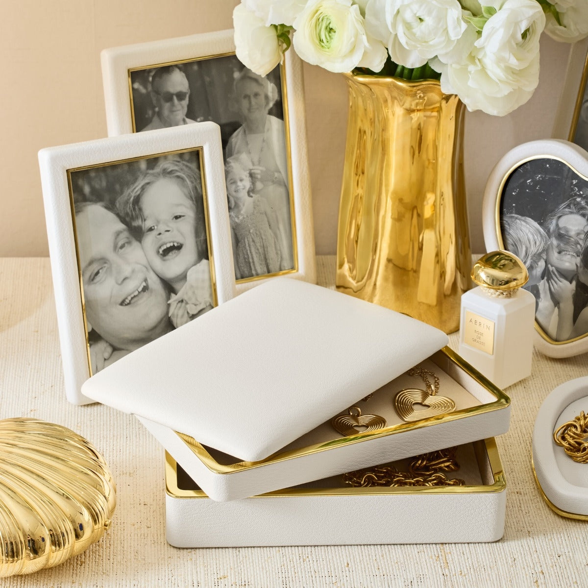 Decorative table setting with gold and white items including a vase, photos, and jewelry.