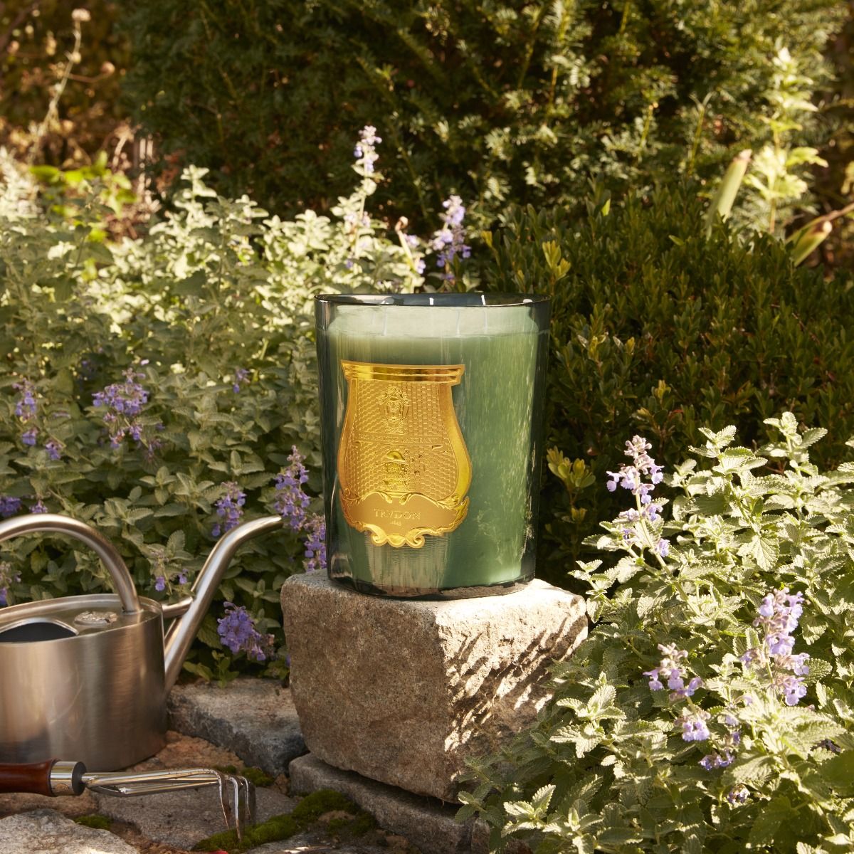 Candle in a decorative holder on a stone block with a garden background