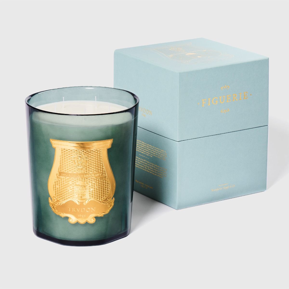 Green candle with gold design next to a matching box on a light gray background