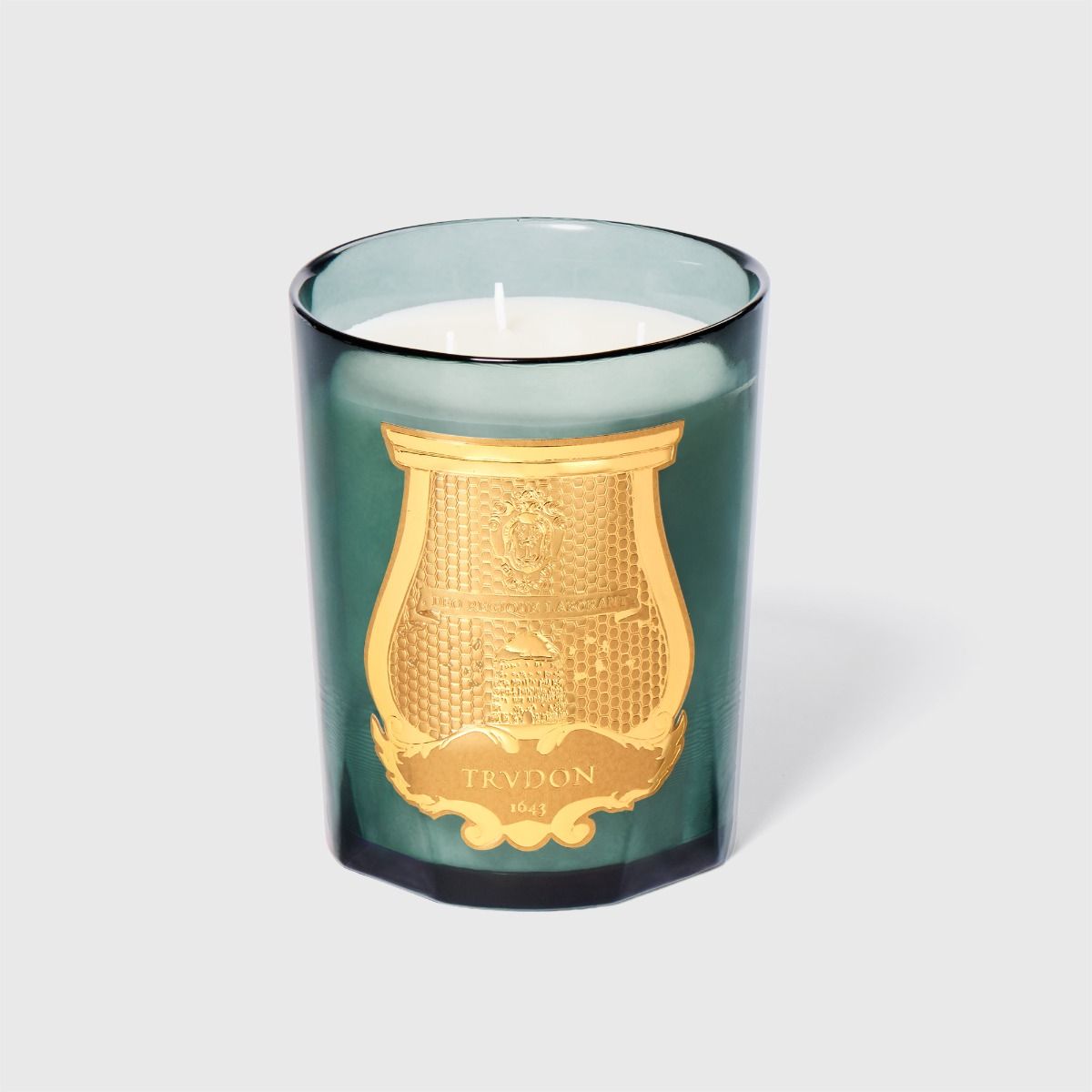 Candle in a green glass container with a gold emblem on a light gray background