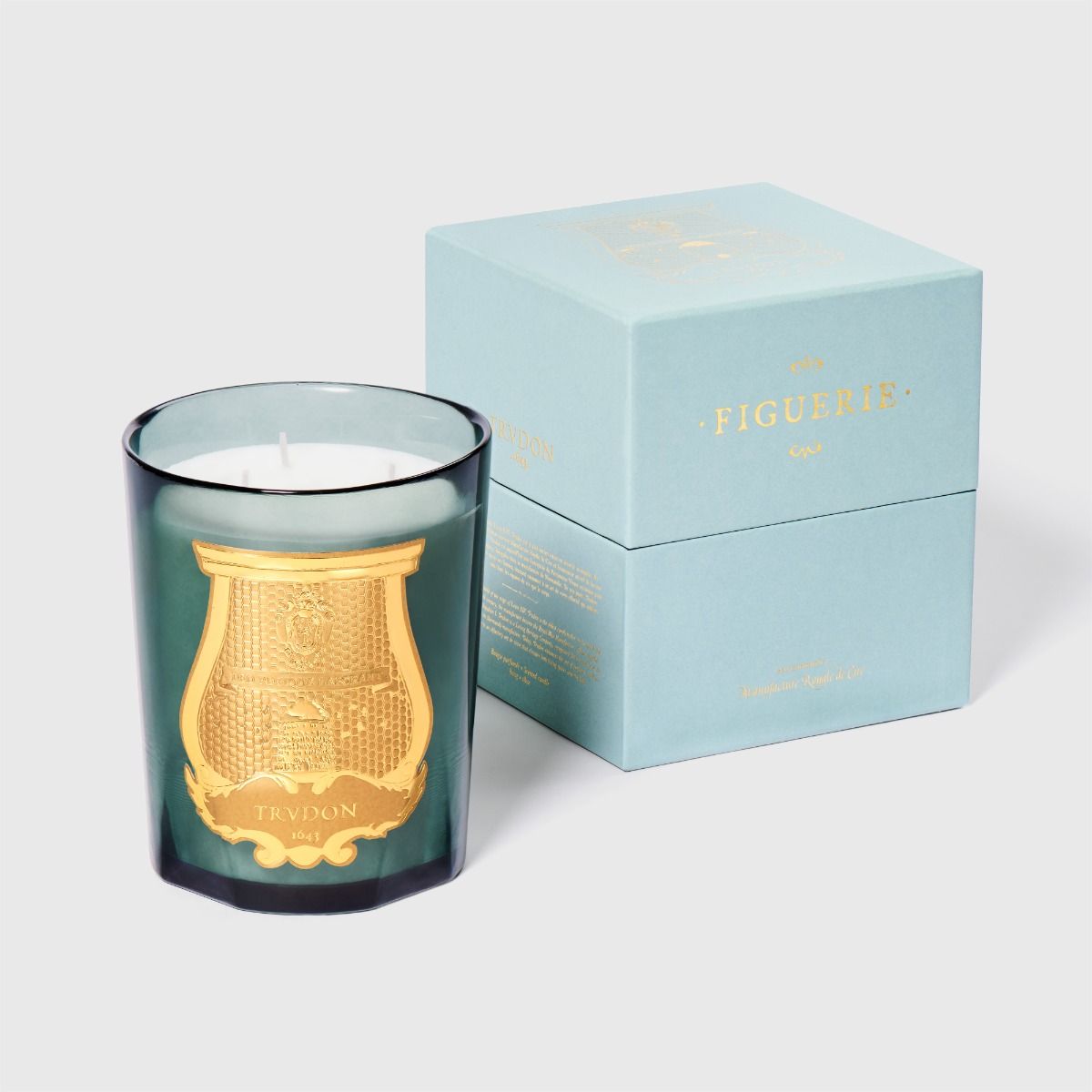 Candle with gold emblem and blue packaging on a light gray background