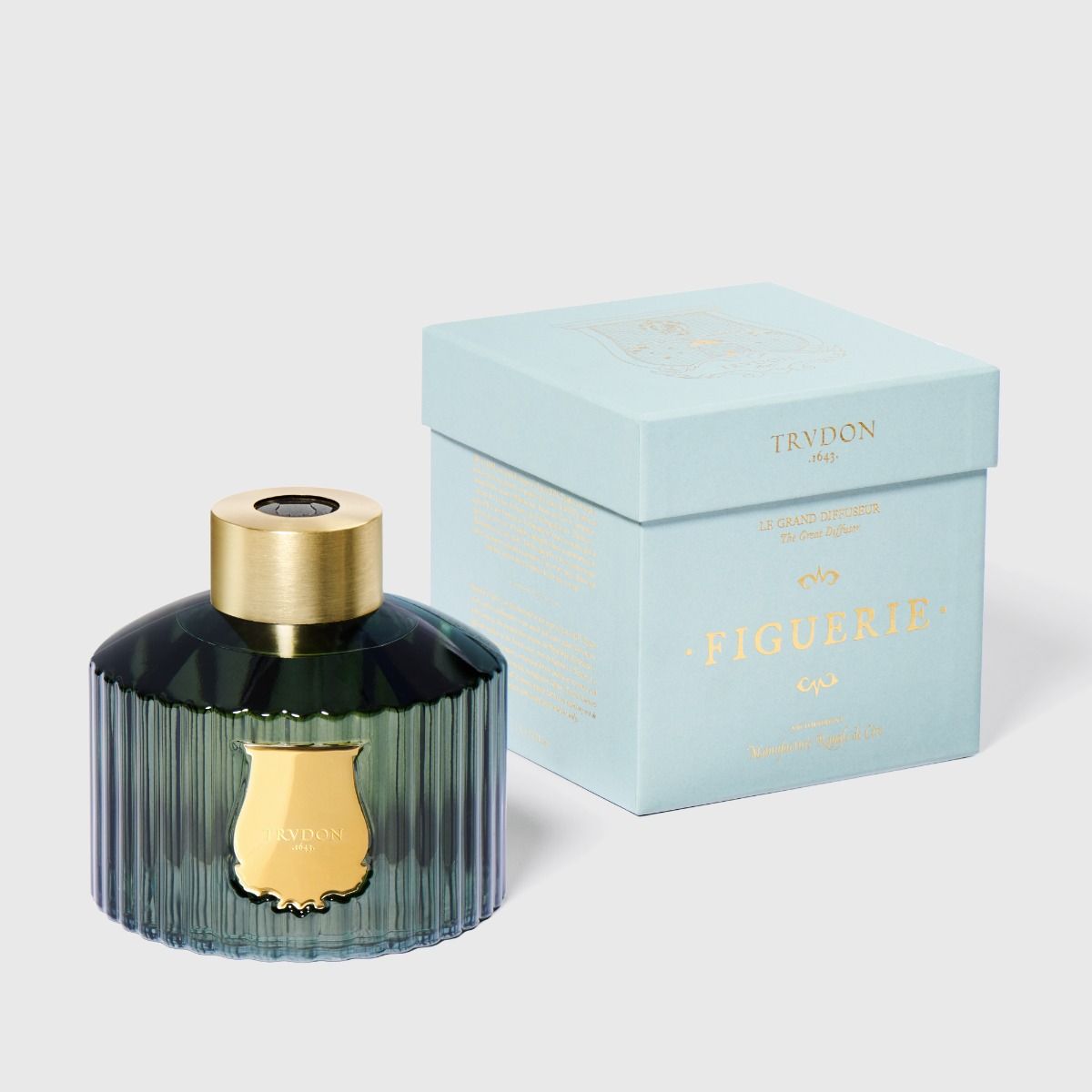 Perfume bottle with gold cap and ribbed design next to its light blue box on a white background
