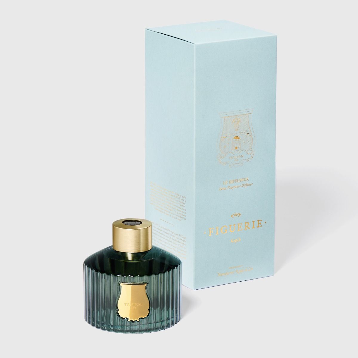 Perfume bottle with gold cap and ribbed design next to its packaging box on a light gray background