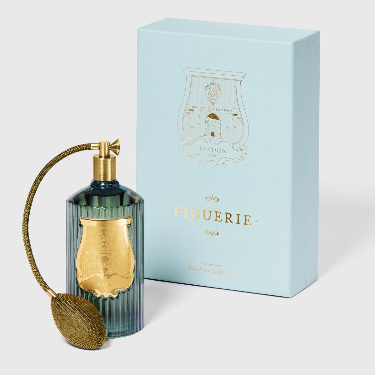 Perfume bottle with gold nozzle and decorative box labeled 'Figuerie' on a light gray background
